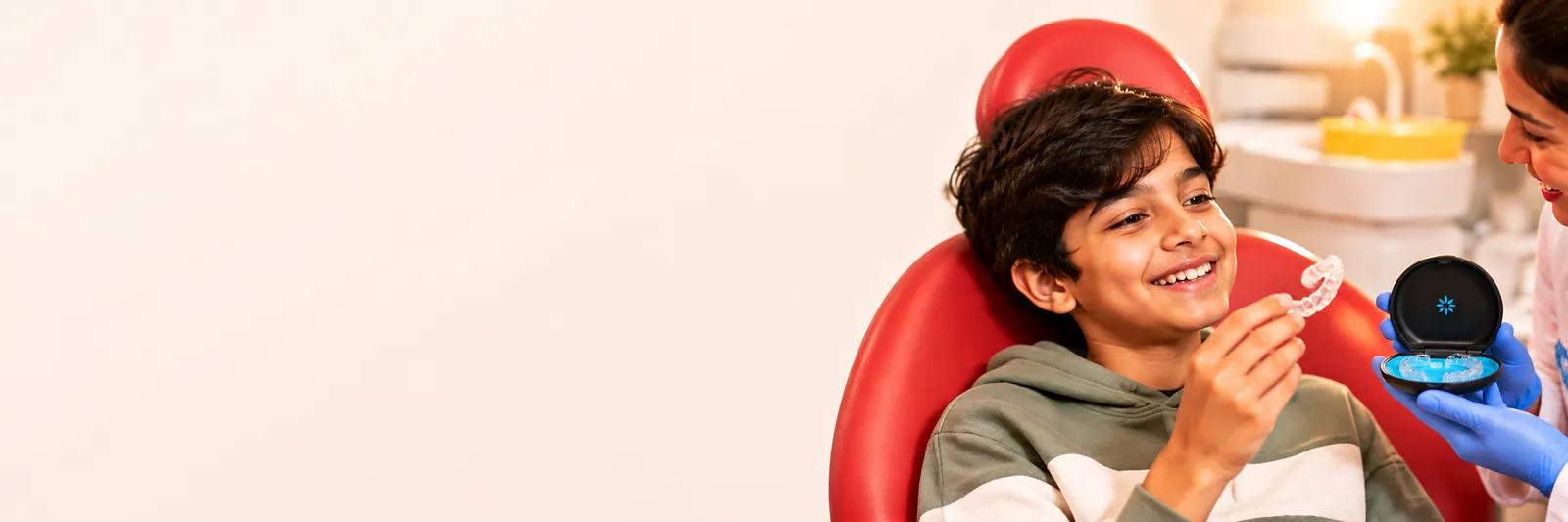 A smiling boy holding a clear aligner while the dentist shows him its case
